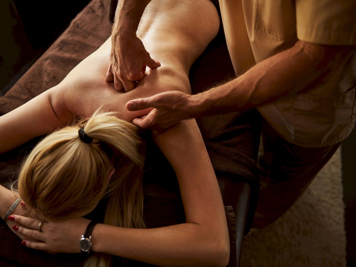 A person receiving a back massage, lying on a massage table with a therapist applying pressure to their upper back.