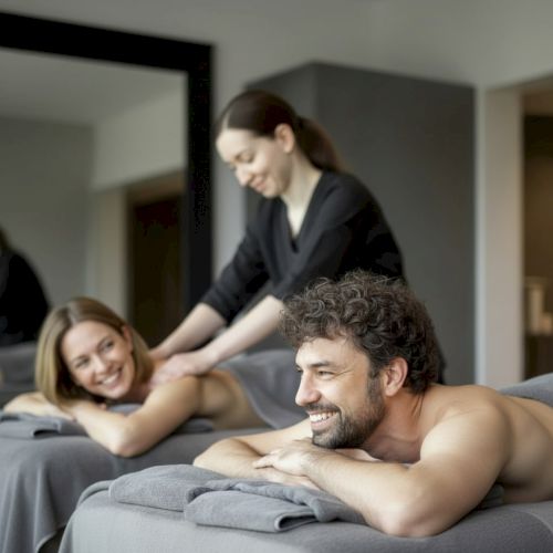 Two people enjoy a couples massage on spa tables while a smiling therapist works in the background.