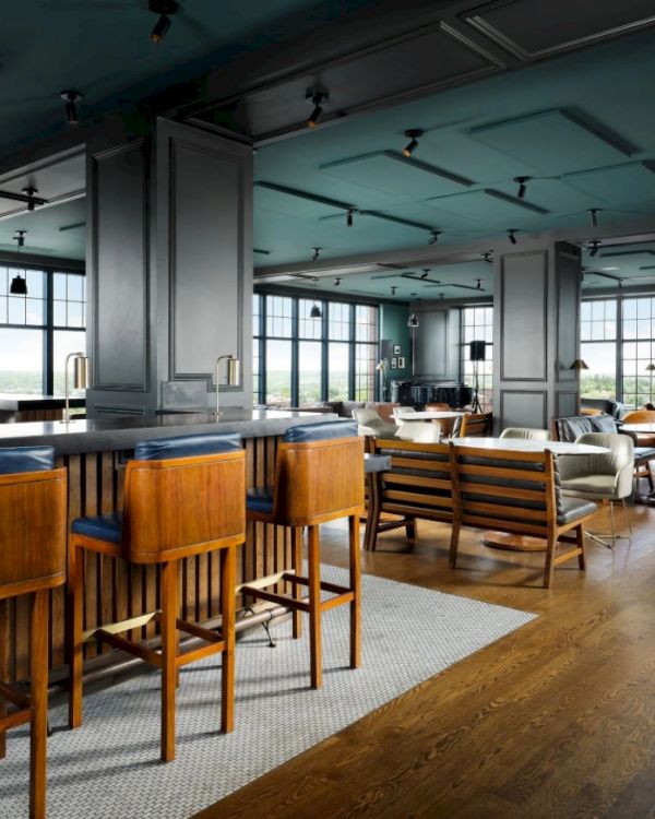 A stylish, airy lounge/bar area with wooden stools, high chairs at a counter, and cozy seating&mdash;bright windows, warm wood tones, modern yet comfy vibe.